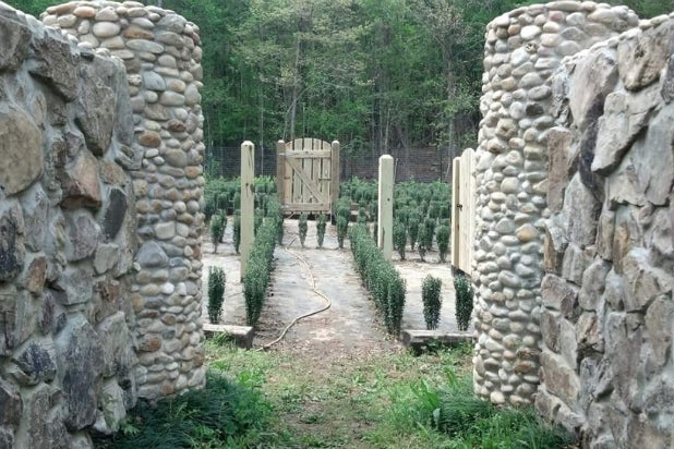 A entrada do labirinto de John com muros de pedra, pequenas roseiras e uma porta de madeira