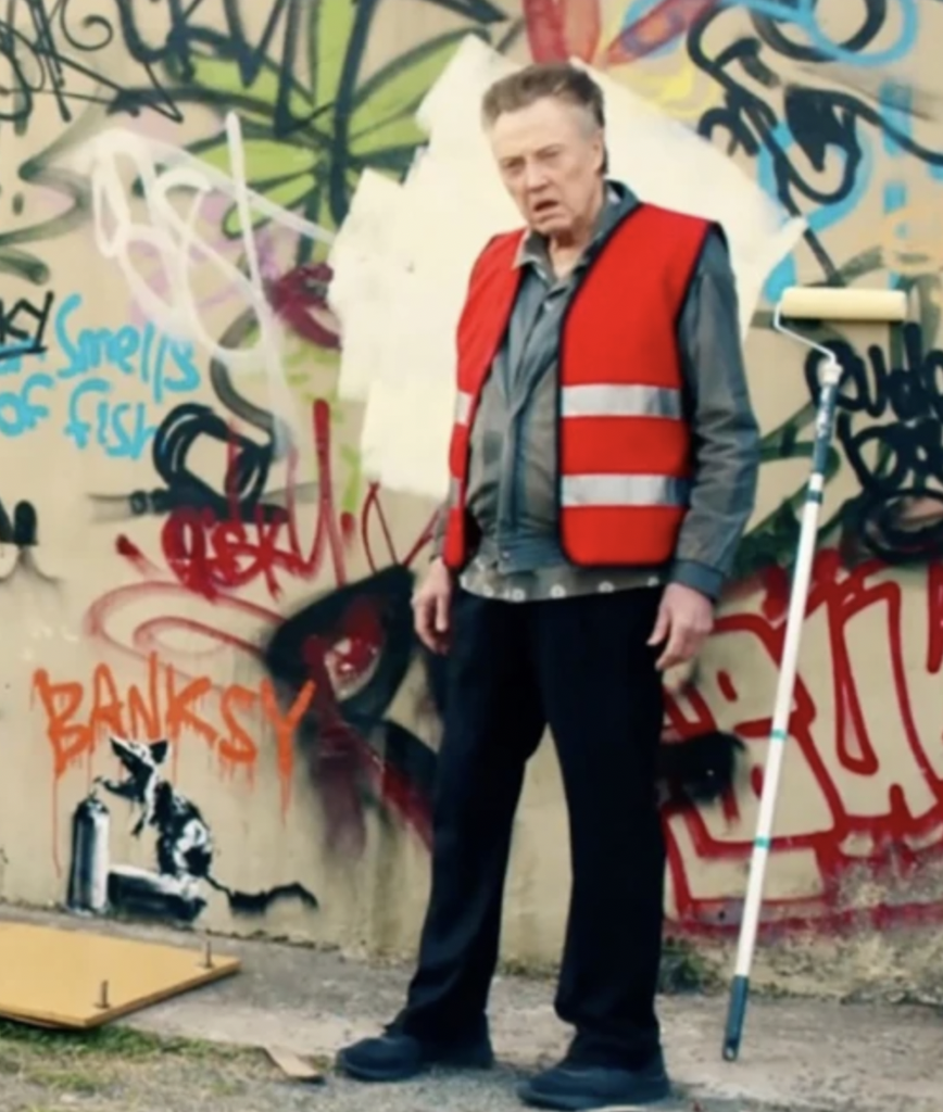 Walken standing in front of Banksy's artwork.