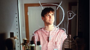 A person stands in front of a mirror with various toiletries on the countertop. They are wearing a red and white striped shirt with a white paper collar and cuffs attached. White lines are drawn on the mirror behind them, resembling a door frame.