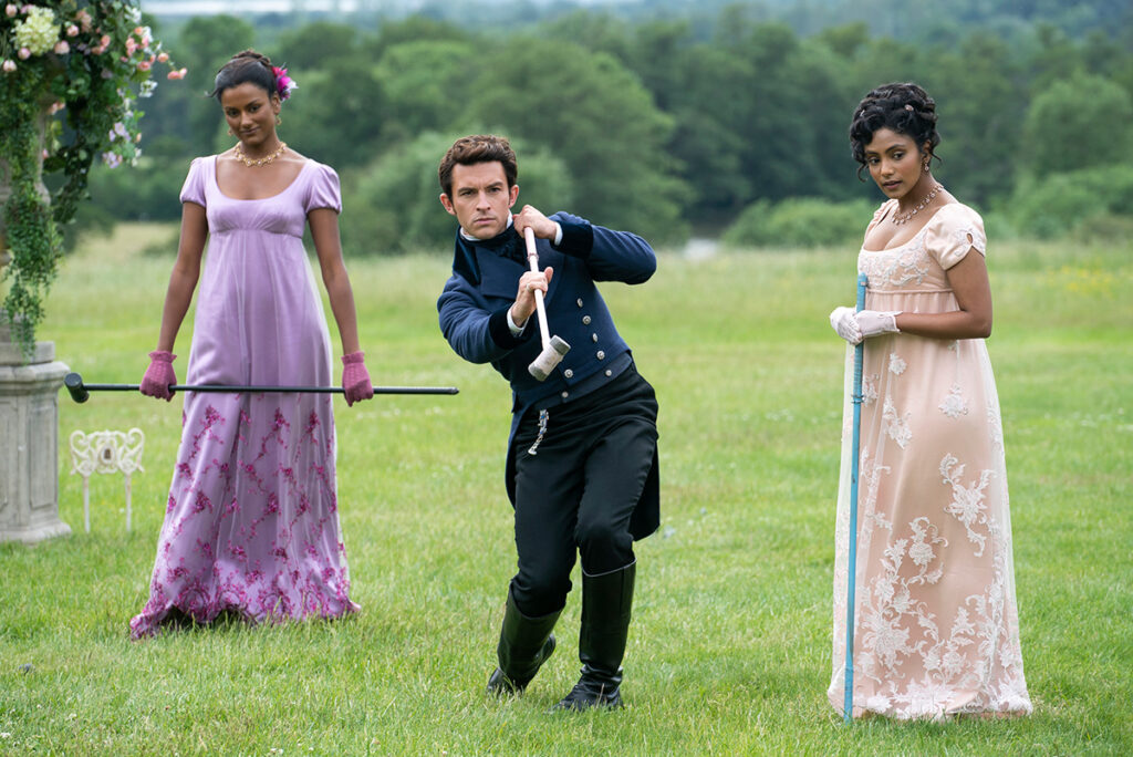 Kate Sharma and Edwina Sharma look on as Anthony Bridgerton takes a shot in the game of pall mall in "Bridgerton" Season 2 (Netflix)