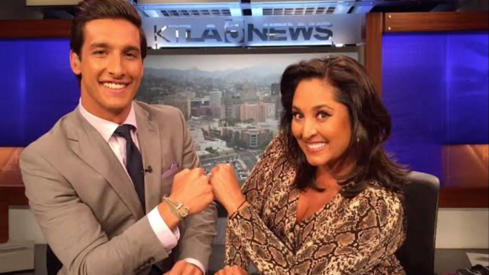 Two television co-anchors, with medium-toned skinn, fist bump.