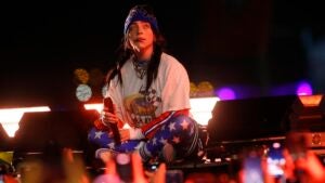 Billie Eilish sits on stage in front of a crowd.