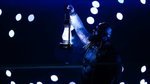 A man stands in a wrestling ring holding up a lamp in the darkness