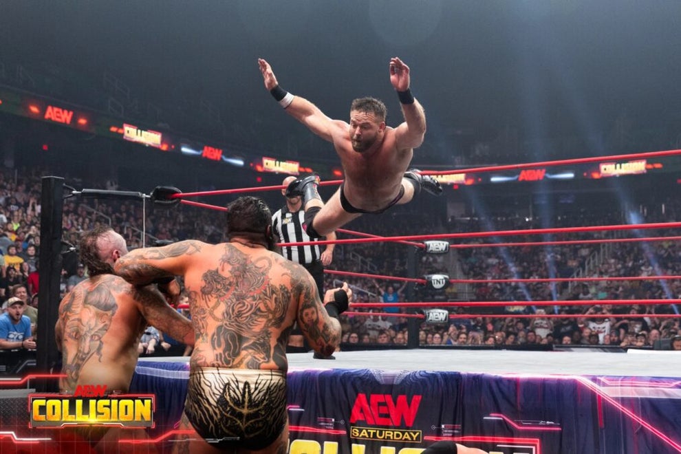 Pro wrestler Dash Wheeler dives through the air onto his opponents out of a pro wrestling ring