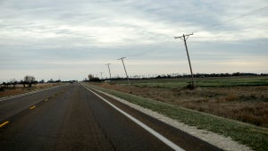 An empty asphalt road, with power lines and grass alongside
