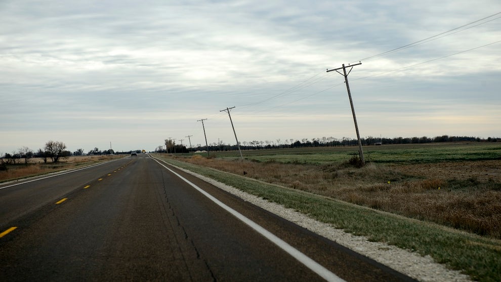 An empty asphalt road, with power lines and grass alongside