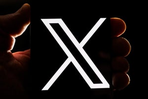 An image of the X logo on a phone, with one leg fatter than the other, the phone being held by a hand.