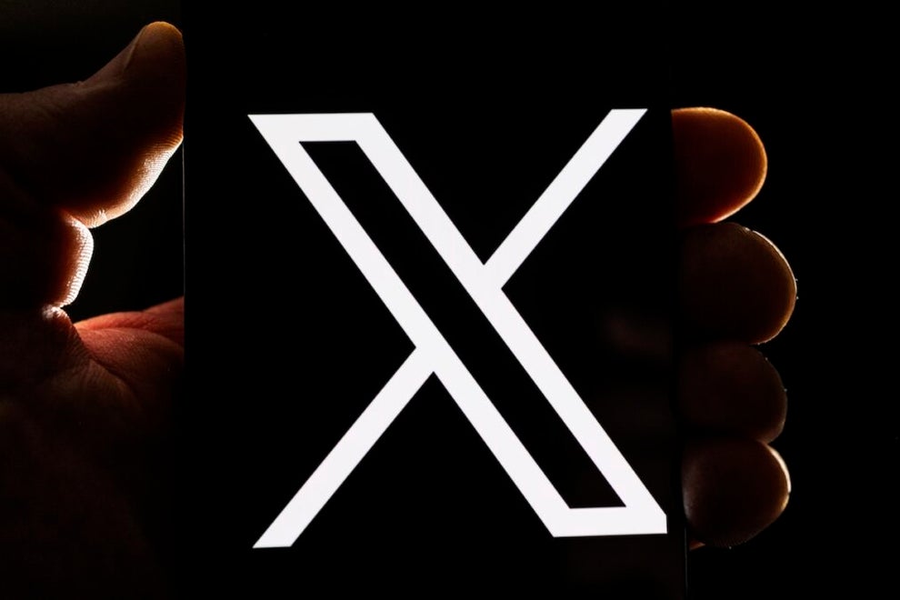 An image of the X logo on a phone, with one leg fatter than the other, the phone being held by a hand.