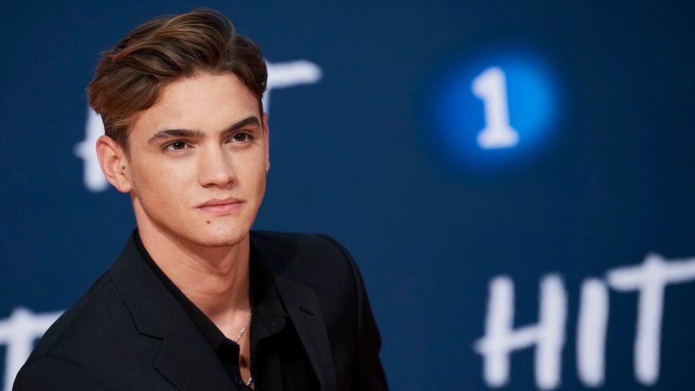 A man with light brown-toned skin gives a stoic look, a blue background with the word "HIT" and the number 1 behind him
