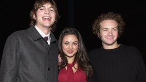 Ashton Kutcher, a tall light-skinned man in a gray jacket, on the left - Mila Kunis, a medium-toned-skinned woman in a red top in the center, and Danny Masterson, a light-skinned man in a black sweater, on the right