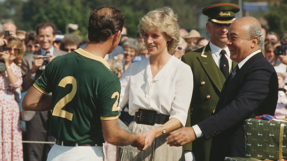Prince Charles, Princess Diana and Mohamed Al Fayed. Charles wears a soccer jersey, Diana in white, older man Mohamed standing nearby smiling, with a man in a Harrods department store uniform behind him.