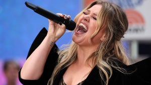 Kelly Clarkson, a woman with light-toned skin, sings with her eyes closed and mouth open in an emotional pose, holding a black microphone as she sings - the mic is wireless. She wears a black outfit with a leopard top underneath. She has highlighted blonde hair and sings in front of an audience — the "Today" logo is in the background, three orange lines resembling a sunrise.