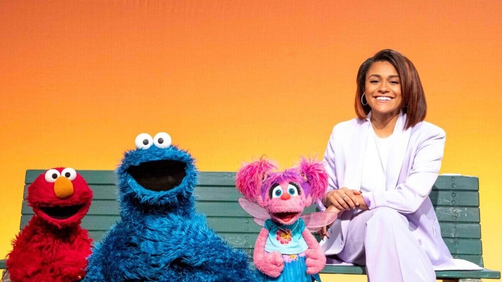 Muppets Elmo, Cookie Monster and Abbey sit on a bench with actress Ariana DeBose