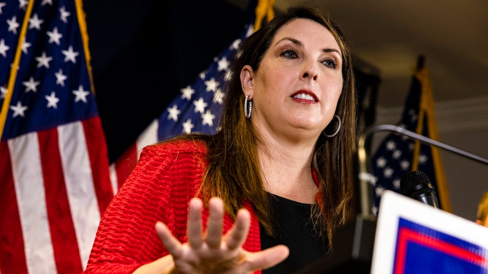 A woman in a red sweater (Ronna McDaniel) speaks at a podium. She has light-toned skin.