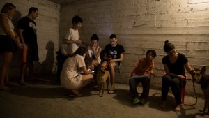 A group of people in a dim shelter, including women, children, and a dog.