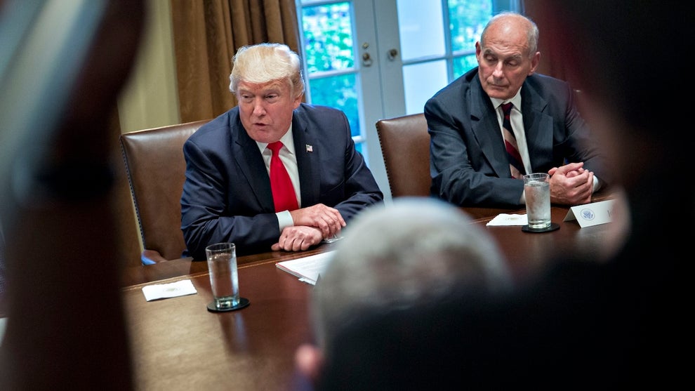 Two men with light-toned skin set at a large conference table, across from people whose faces are unseen in the foreground. The man on the right looks to the man on the left, who wears a bright red tie and appears to be speaking. The man on the left is then-President Donald Trump.