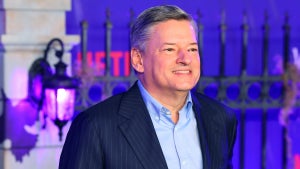 A man with light-toned skin and gray hair stands in front of a wrought iron fence with a NETFLIX logo behind him.