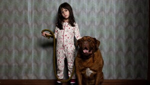 A little girl stands next to a large dog, holding his leash and looking direct into camera in still photo from "When Evil Lurks"