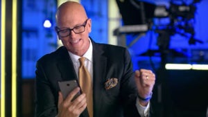 A bald man holding a smart phone with one hand pumps his other fist.