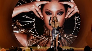 A woman with dark-toned skin stands in front of a backdrop of herself in front of a large crowd.