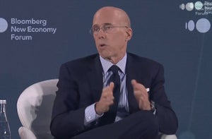 Jeffrey Katzenberg, a bald man wearing a suit, gestures while he speaks. A sign on the wall behind him says "Bloomberg New Economy Forum."