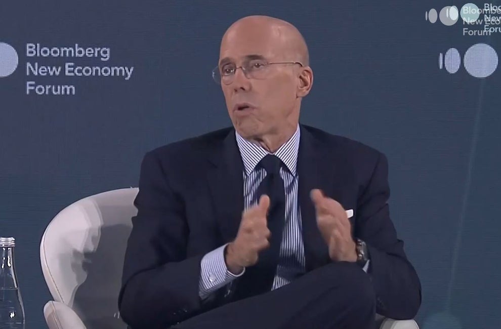 Jeffrey Katzenberg, a bald man wearing a suit, gestures while he speaks. A sign on the wall behind him says "Bloomberg New Economy Forum."