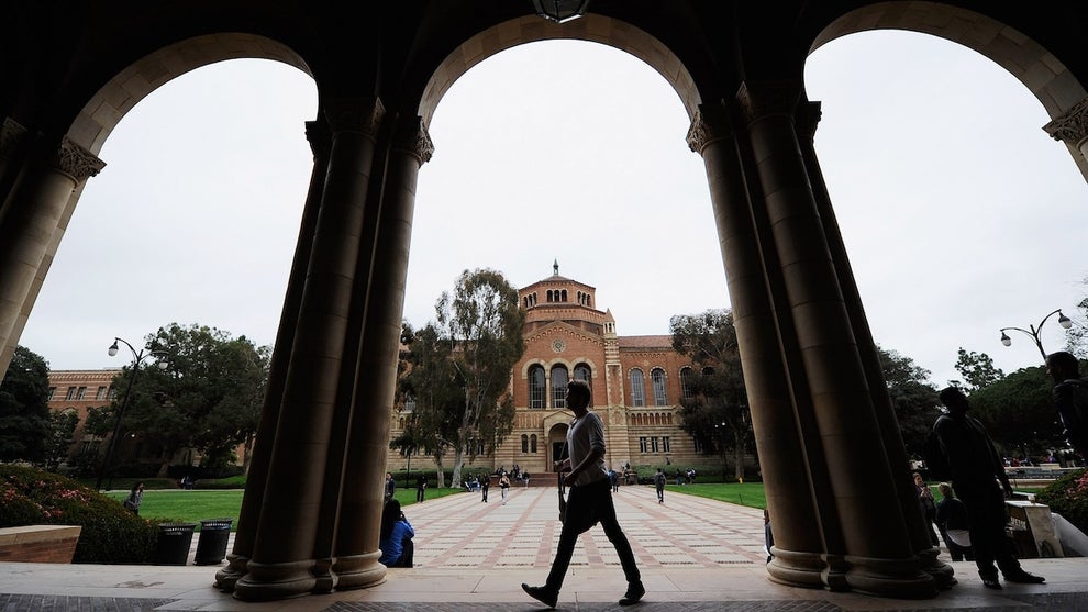 An outdoor shot showing a person walking beneath tall arches, framed around a campus building that appeared to be made of brick in the background.