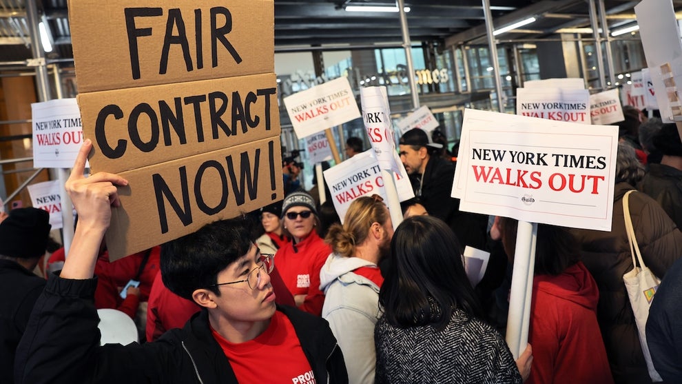 A group of people picket, including one holding a "FAIR CONTRACT NOW" sign and another with a sign reading "NEW YORK TIMES WALKS OUT"
