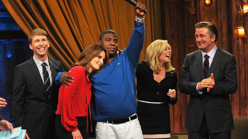 A group of people including two white women, and three men (two white, one Black) stand on stage sharing a happy moment.