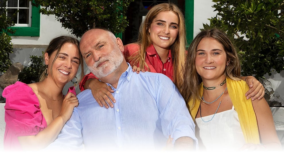 An older man with younger women smiling around him; they all have light-medium-toned skin.