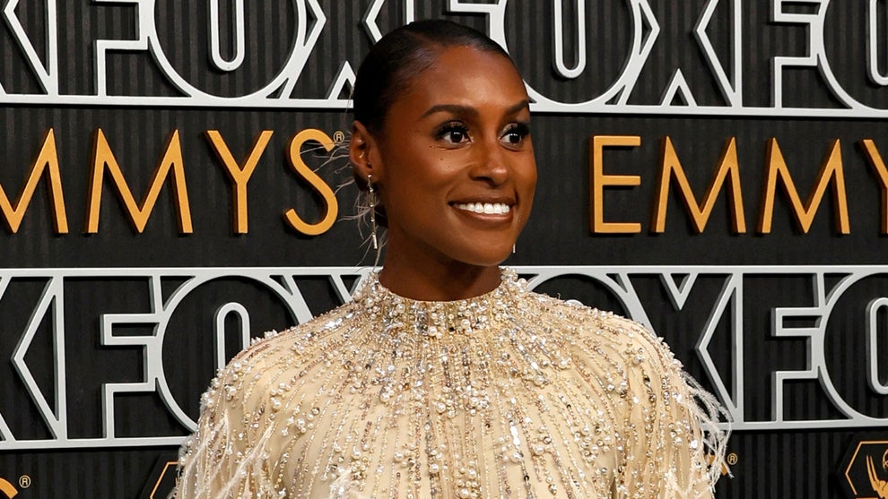 A Black woman smiles in front of a bcakdrop for the Emmys