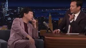 Ken Jeong, "Community" alum, an Asian man with medium-toned skin, sits at a couch across from a desk where a man with light-toned skin, Jimmy Fallon, sits.