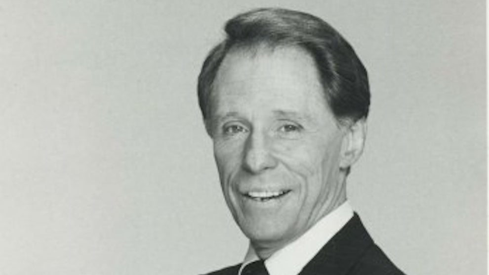 An older man, John Hamlin, with light-toned-skin poses, wearing a suit.