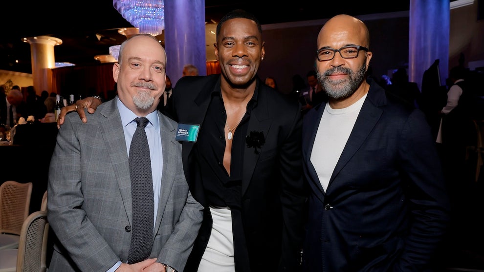 One light-skinned man and two taller Black men pose for a photo. They all wear suits, standing in a dimly lit ballroom.