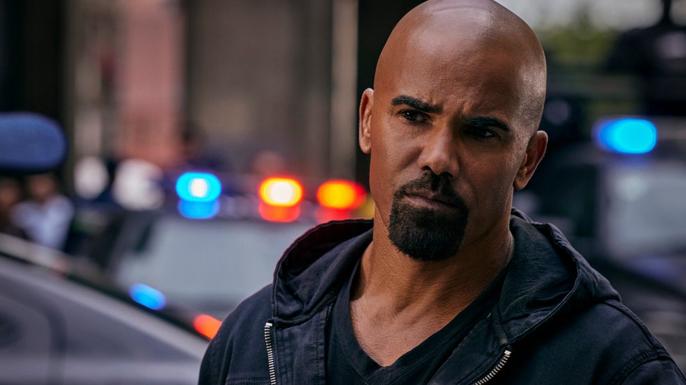 Shemar Moore wears a hoodie and stands in front of flashing police lights in a still image from SWAT season 7