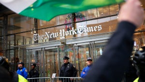 Protesters outside of the New York Times offices, guarded by police, as one protesters waves a Palestinian flag.