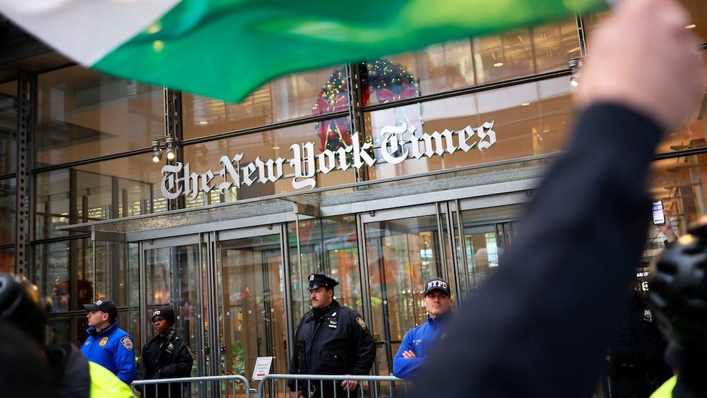 Protesters outside of the New York Times offices, guarded by police, as one protesters waves a Palestinian flag.