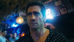 Jake gyllenhaal stands in front of a neon-lit bar in Road House