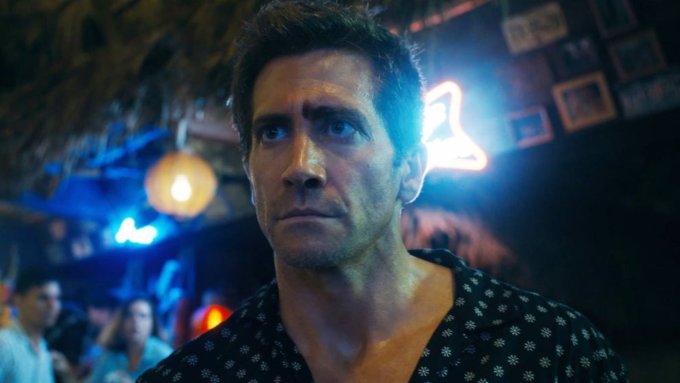 Jake gyllenhaal stands in front of a neon-lit bar in Road House