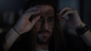 A man looks with despair at his computer, holding his hands up by his head. He has light-toned skin and looks disheveled.