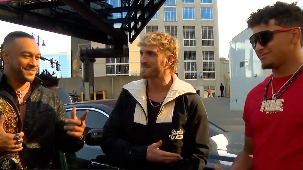 Men with medium-toned skin on either side, a man with light-toned skin in the middle, standing outside in a parking lot next to a black car. The men are Damian Priest, Logan Paul and Patrick Mahomes.