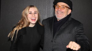 A young woman with her older father. They look happy and both have light-toned skin. They wear black outfits.