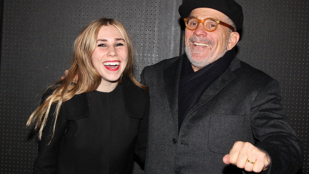 A young woman with her older father. They look happy and both have light-toned skin. They wear black outfits.