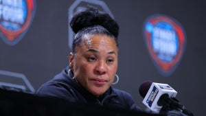 A Black woman sits in front of a microphone, appearing skeptical.