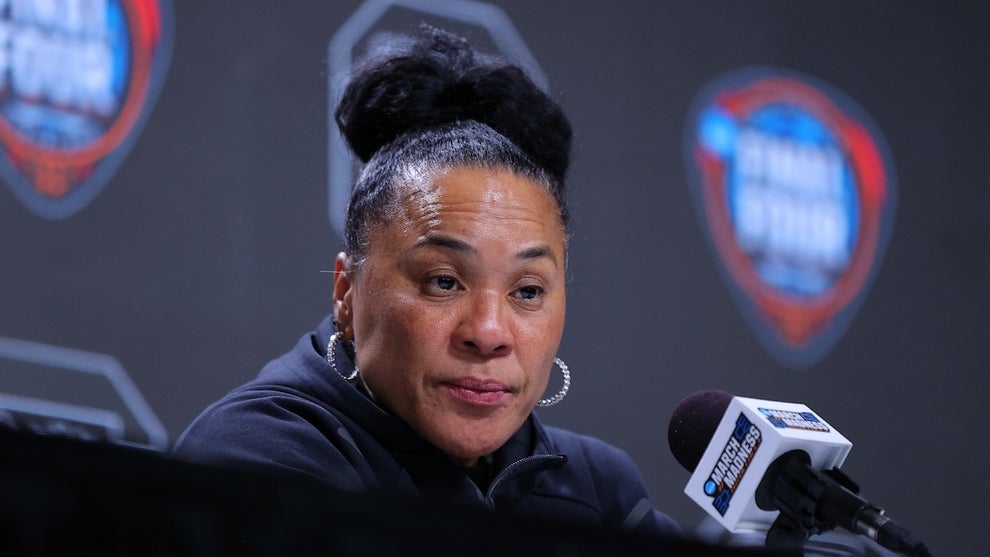 A Black woman sits in front of a microphone, appearing skeptical.