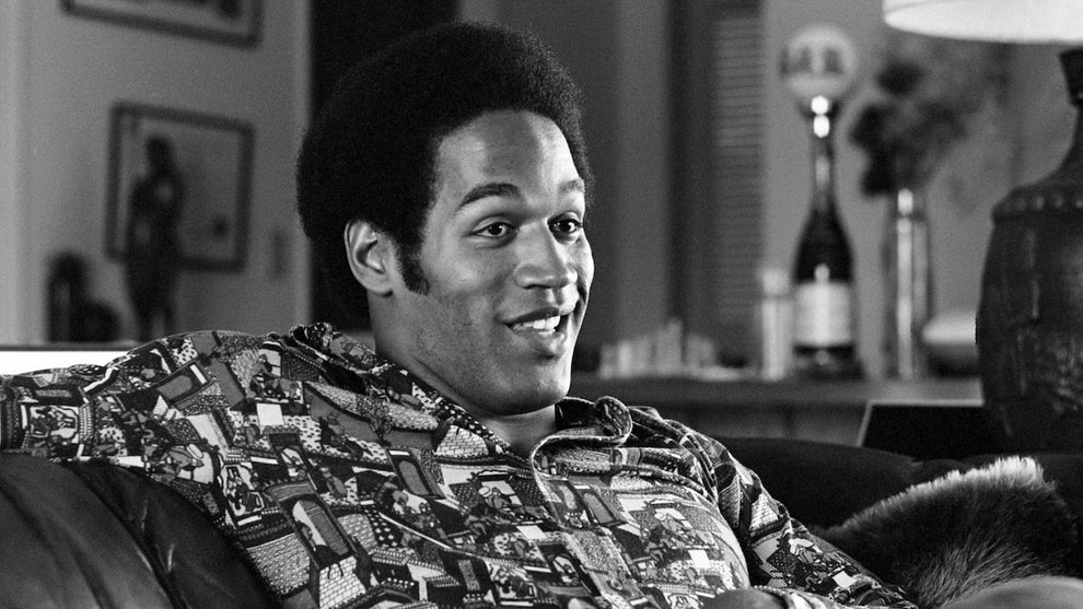 A Black man smiles as he sits, relaxing on a couch.