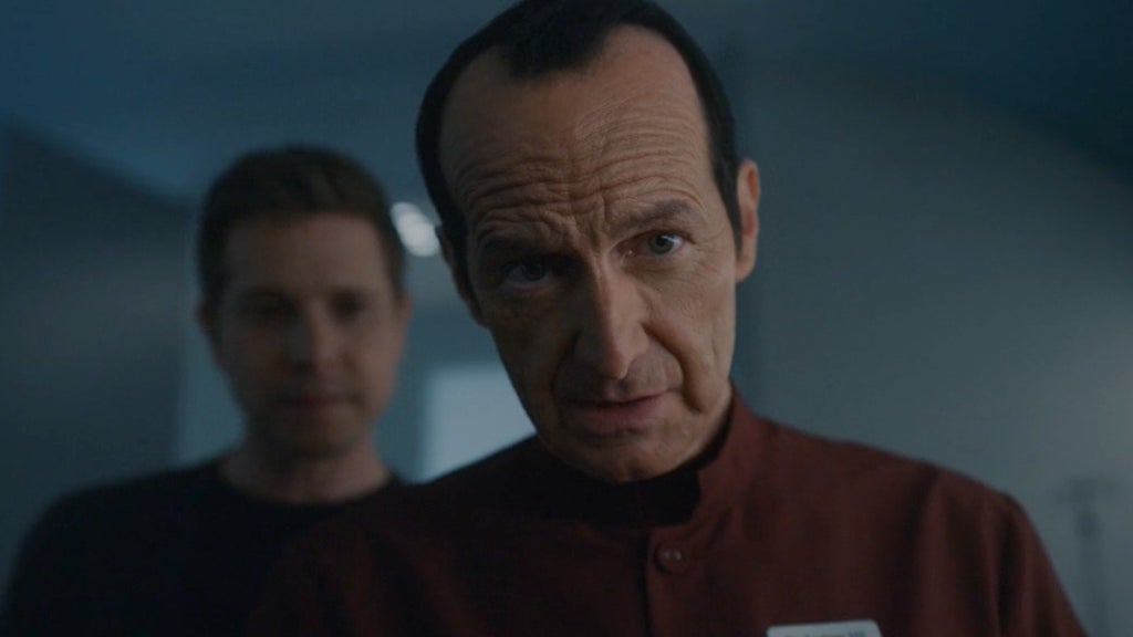 Denis O'Hare wears red doctor's scrubs and looks directly into the camera in American Horror Story: Delicate