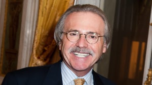 An older man with a silver mustache smiles, wearing a suit, in a ballroom-styled environment.