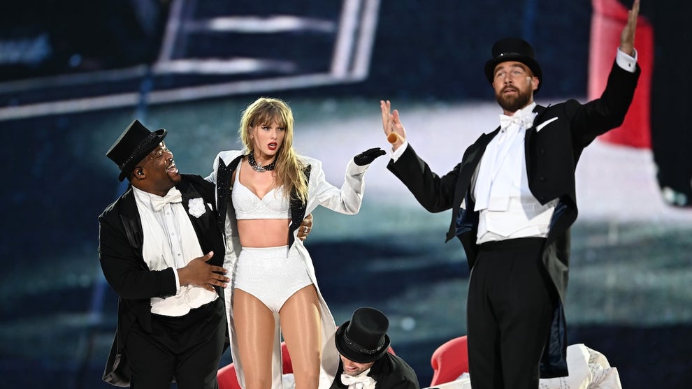 A woman is joined onstage by several men in tuxedoes. There is one Black man and two with lighter skin.