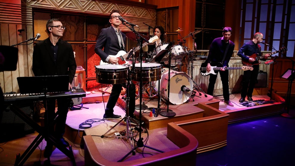 A band plays on stage on a talk show TV set.